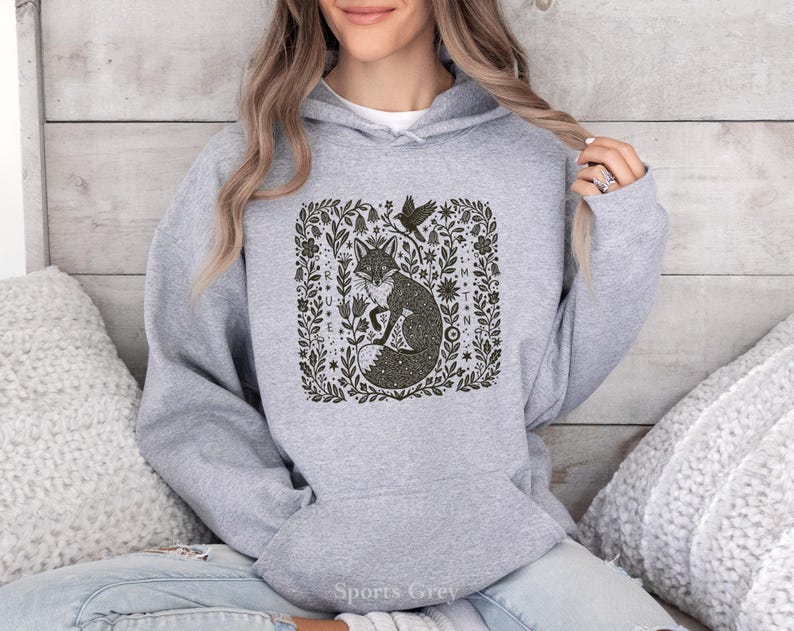 May include: A grey hoodie featuring a dark green illustration of a fox within a floral frame, with a bird. The hoodie has a drawstring hood and a front pocket. The text "Sports Grey" is visible at the bottom.
