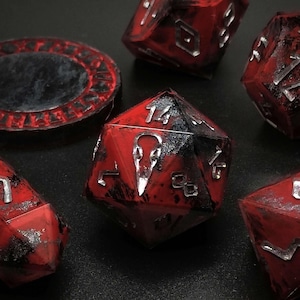 May include: Set of seven red and black dice with silver metallic numbers and symbols. The dice are on a black surface.