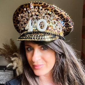 May include: A leopard print hat with gold and black accents, adorned with sparkling rhinestones and the number "40". The hat features a studded brim and is embellished with various decorative elements, creating a festive and celebratory look.