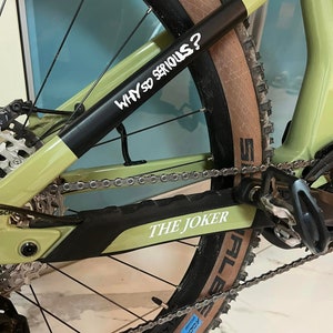 May include: A green mountain bike with black tires and a chain. The bike has a black sticker on the frame that says "WHY SO SERIOUS?" and another sticker that says "THE JOKER".