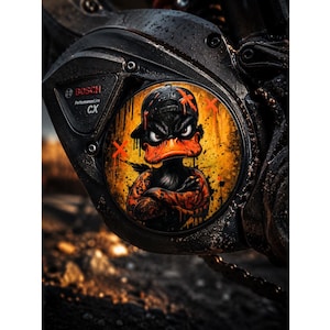 Könnte beinhalten: Eine schwarze Bosch Performance Line CX Motorabdeckung mit einer kreisförmigen Grafik einer Cartoon-Ente mit Baseballkappe. Die Ente hat einen wütenden Ausdruck, verschränkte Arme und ist vor einem gelb-orangen Graffiti-Hintergrund abgebildet.