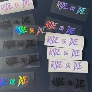 Könnte beinhalten: Eine Sammlung von Aufklebern mit dem Text "RIDE OR DIE" in verschiedenen Farben und holografischen Effekten. Die Aufkleber befinden sich auf transparentem Trägermaterial und sind auf einer dunkelblauen Oberfläche angeordnet.
