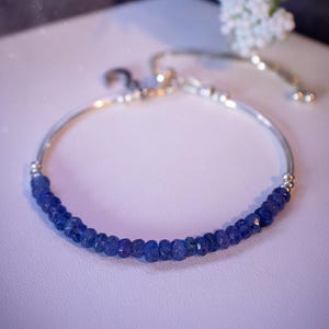 May include: A silver bracelet with a blue gemstone bead chain. The bracelet has a sliding clasp for adjusting the fit.
