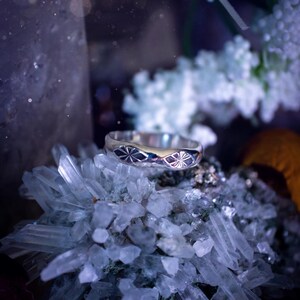 May include: A silver ring featuring a delicate floral design, set against a backdrop of clear quartz crystals.