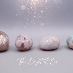 May include: Four smooth, polished agate stones in shades of pink, white, and blue. The stones are arranged in a row on a grey surface. The Crystal Co. is written in white script below the stones.