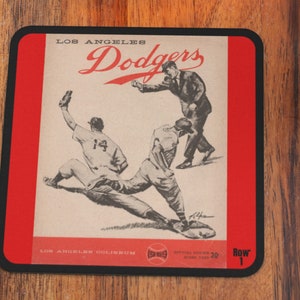 May include: A vintage Los Angeles Dodgers ticket stub with a black border and red background. The ticket stub features a black and white illustration of three baseball players. The text "Los Angeles Dodgers" is printed in black at the top of the ticket stub. The text "Los Angeles Coliseum" is printed in black at the bottom of the ticket stub. The text "Row 1" is printed in black at the bottom right corner of the ticket stub.