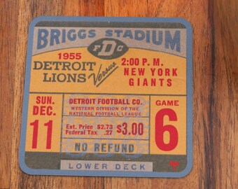 May include: A vintage ticket stub for a 1955 Detroit Lions football game at Briggs Stadium. The ticket is yellow with red and blue text and reads "Detroit Lions Versus New York Giants" and "Game 6".