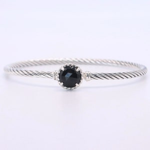 May include: A silver-toned bangle bracelet with a twisted rope design. The bracelet features a central, round, black gemstone. The gemstone is set in a decorative bezel setting, adding a touch of elegance to the jewelry.