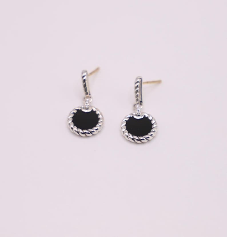 Puede incluir: Un par de pendientes de plata con piedras de &oacute;nix negro y un dise&ntilde;o de cuerda trenzada.