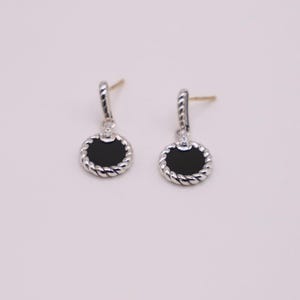 Puede incluir: Un par de pendientes de plata con piedras de &oacute;nix negro y un dise&ntilde;o de cuerda alrededor del borde de las piedras.