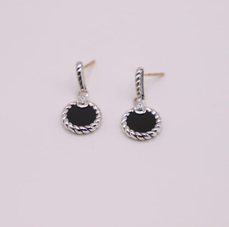 Puede incluir: Un par de pendientes de plata con piedras de &oacute;nix negro y un dise&ntilde;o de cuerda alrededor del borde de las piedras.