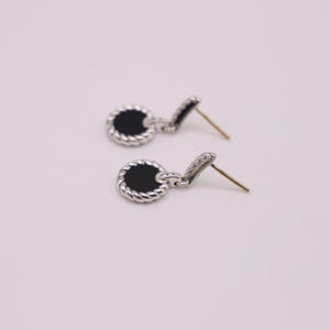 Puede incluir: Un par de pendientes de plata con piedras de &oacute;nix negro. Los pendientes tienen un dise&ntilde;o de cuerda alrededor de las piedras.