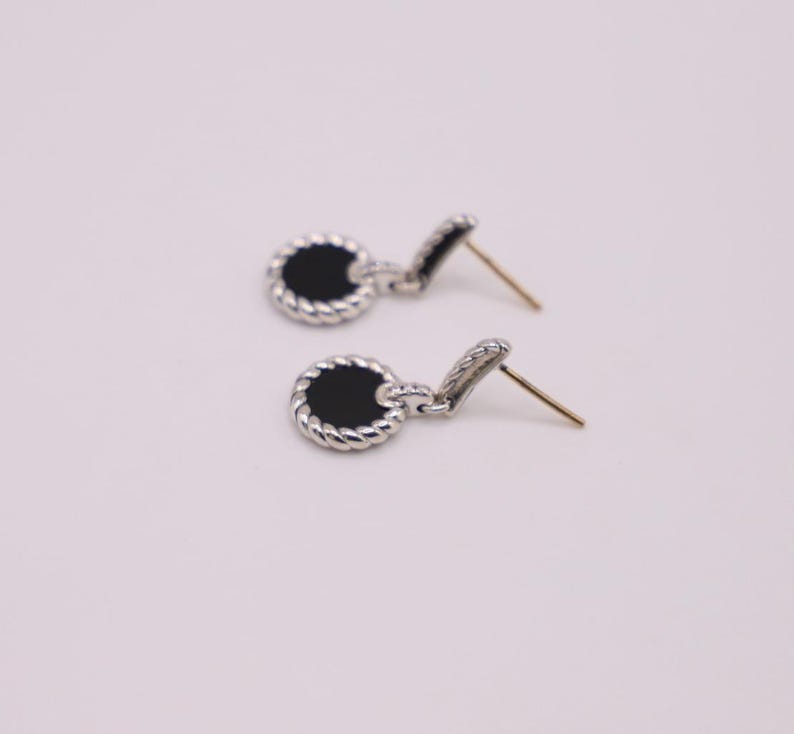 Puede incluir: Un par de pendientes de plata con piedras de &oacute;nix negro. Los pendientes tienen un dise&ntilde;o de cuerda alrededor de las piedras.