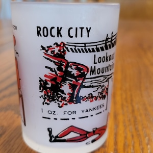 May include: White frosted glass shot glass with a red and black illustration of a person running. The text "Rock City Lookout Mountain 1 oz. for Yankees" is printed on the glass.