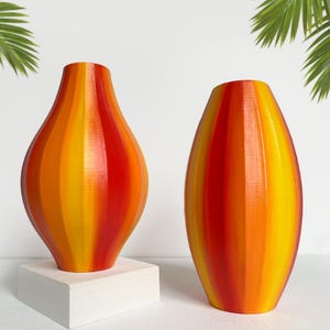 May include: Two ceramic vases with a striped pattern in shades of red, orange, and yellow. The vases are on a white surface.