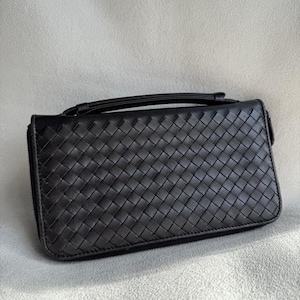 May include: A black rectangular clutch wallet featuring a woven leather exterior pattern. The accessory includes a top handle strap and a full-length zipper closure along the side, providing a structured and uniform appearance for daily use.