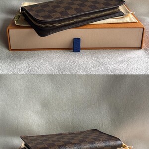 May include: A brown leather wallet with a checkered pattern and a gold zipper. The wallet is in a brown box with a blue ribbon.