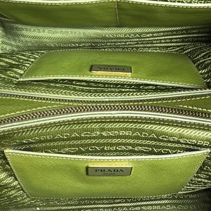 May include: Close-up of a green Prada handbag interior. The bag features multiple compartments with a light green lining and the Prada logo. The interior is detailed with the Prada logo pattern.