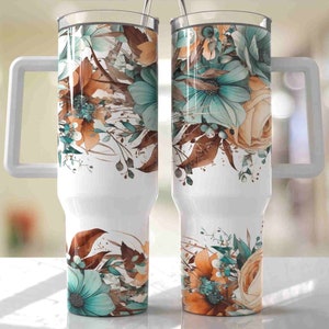 Op de afbeelding: Twee witte ge&iuml;soleerde bekers met handvatten, elk versierd met een bloemenontwerp. Het ontwerp toont turquoise, oranje en bruine bloemen en bladeren tegen een witte achtergrond. De bekers hebben doorzichtige deksels en metalen rietjes.