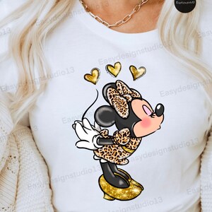 May include: A white t-shirt with a cartoon image of Minnie Mouse wearing a leopard print dress and gold glitter shoes. Three gold hearts are above her head.