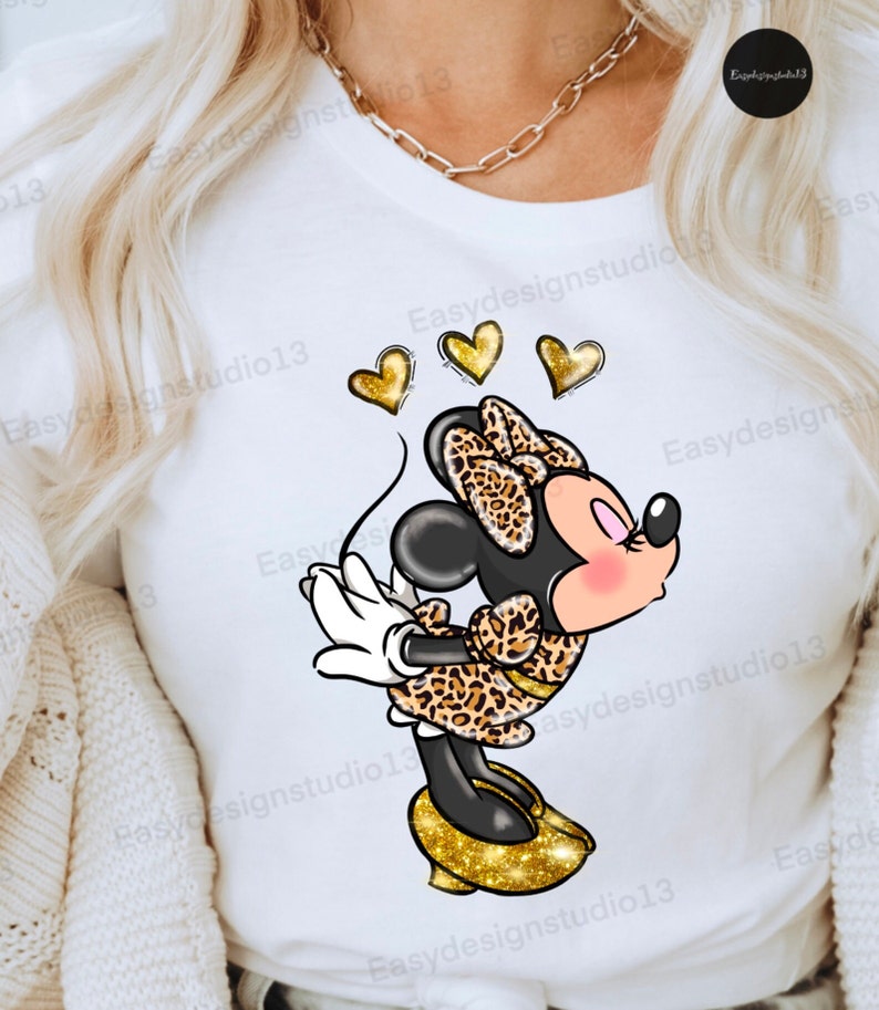 May include: A white t-shirt with a cartoon image of Minnie Mouse wearing a leopard print dress and gold glitter shoes. Three gold hearts are above her head.