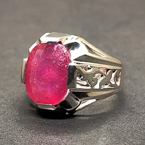 May include: A silver ring with a large, oval-shaped, pink gemstone set in the center. The ring has a detailed, filigree design on the band.