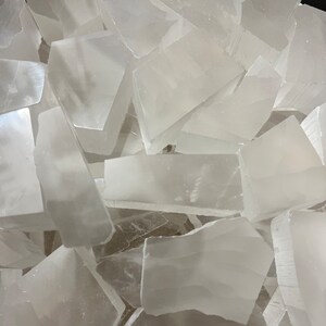 Peut inclure: Un tas de morceaux de cristal de s&eacute;l&eacute;nite blanche. Les cristaux sont translucides et ont une surface lisse et polie.