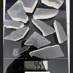 Peut inclure: Une balance num&eacute;rique affichant 455 grammes avec une collection de morceaux de cristal de s&eacute;l&eacute;nite clairs et bris&eacute;s sur une surface noire. Le texte "Approx 1lb smaller pieces" est sous la balance.