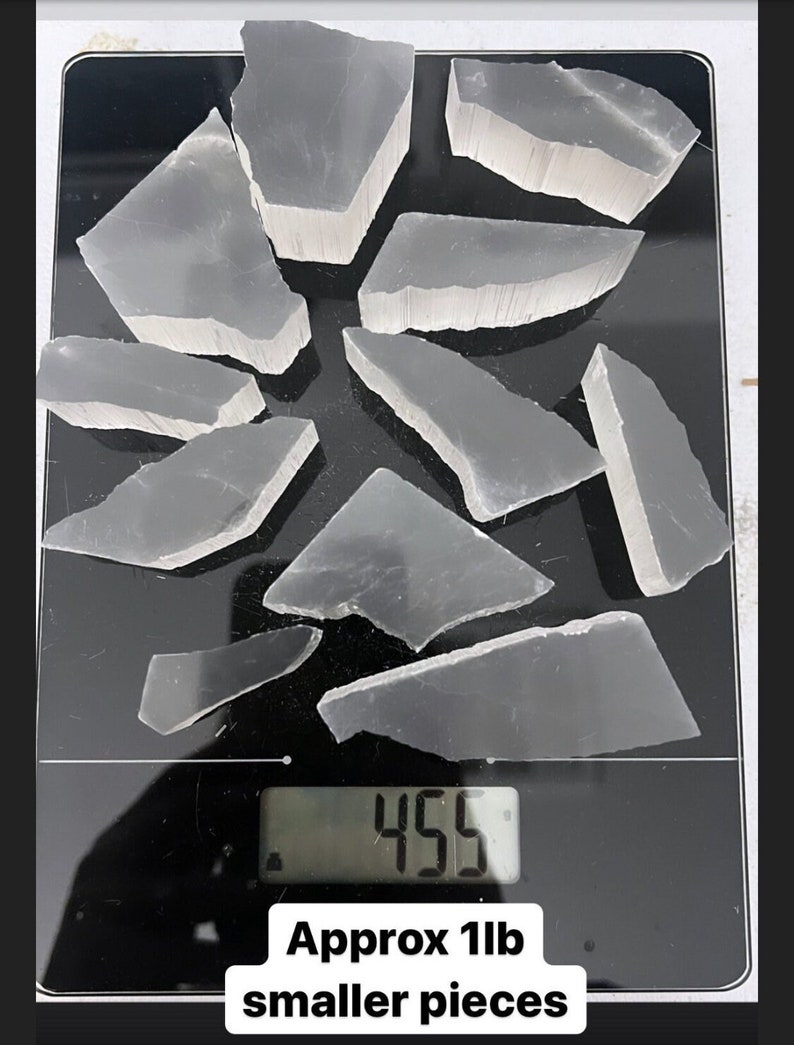 Peut inclure: Une balance num&eacute;rique affichant 455 grammes avec une collection de morceaux de cristal de s&eacute;l&eacute;nite clairs et bris&eacute;s sur une surface noire. Le texte "Approx 1lb smaller pieces" est sous la balance.
