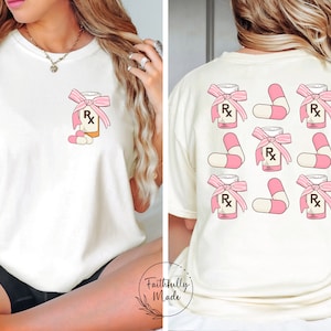 May include: A white t-shirt with a pink pill bottle and pills printed on the front. The back of the shirt has a pattern of nine pink pill bottles and pills.