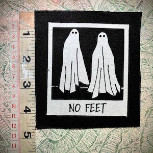 Op de afbeelding: Zwart vierkantige patch met een witte lijst, met twee spookfiguren met stipogen en vloeiende gewaden. De tekst "NO FEET" is eronder gedrukt. De patch meet ongeveer 12,7 cm in het vierkant.