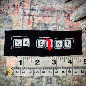 Può includere: Toppa in tessuto nero con lettere bianche che compongono la parola "Y, A, C, N, T" su sfondo nero. La toppa è lunga circa 10 cm.
