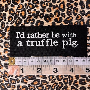 May include: A rectangular black fabric patch with white embroidered text that reads, "I'd rather be with a truffle pig." A measuring tape is positioned below the patch, showing a width of approximately 5 inches.