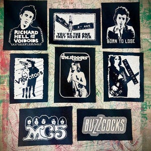 May include: A collection of black and white patches featuring various punk rock band logos and portraits. Bands include Richard Hell and the Voidoids, The Stooges, and Buzzcocks. The patches are rectangular and have white text and graphics.