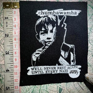 以下が含まれることがあります： 黒い正方形のパッチ。白いグラフィックは、ピースサインをしている人物です。「chumbawamba」のテキストが上にあり、「WELL NEVER REST AGAIN UNTIL EVERY NAZI goes away」が下にあります。