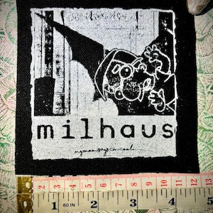 Puede incluir: Un parche en blanco y negro con un personaje de dibujos animados y la palabra "milhaus". El parche tiene un borde negro y el texto "my mom says I'm cool" está escrito debajo de la palabra "milhaus". El parche mide aproximadamente 10 cm de ancho.