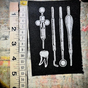 May include: Black and white embroidered patch with a tooth and dental tools, including a syringe, a mirror, and two picks.