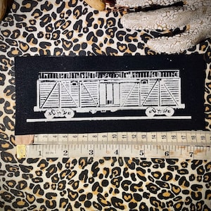 Op de afbeelding: Een zwarte patch met een witte illustratie van een vintage treinwagon. De patch is ongeveer 15 cm lang. De achtergrond is een luipaardprint stof. Een meetlint is eronder geplaatst.