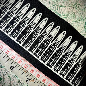 May include: Black fabric patch with a white outline of a row of bullets. The patch is approximately 22 inches long.