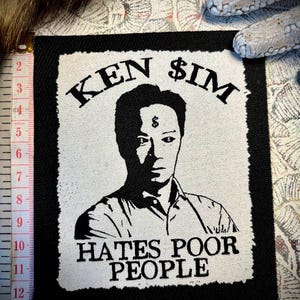 Può includere: Una toppa rettangolare in bianco e nero con un ritratto stilizzato e il testo "KEN $IM" sopra e "HATES POOR PEOPLE" sotto. Lo sfondo è bianco.