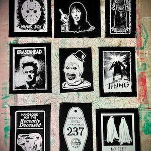 Puede incluir: Nueve parches en blanco y negro con imágenes de películas de terror y cultura pop. Los diseños incluyen una máscara de hockey, una mujer con un cigarrillo, un monstruo con sombrero de copa, la palabra "Eraserhead", un payaso, un monstruo, una llave de hotel y dos fantasmas.