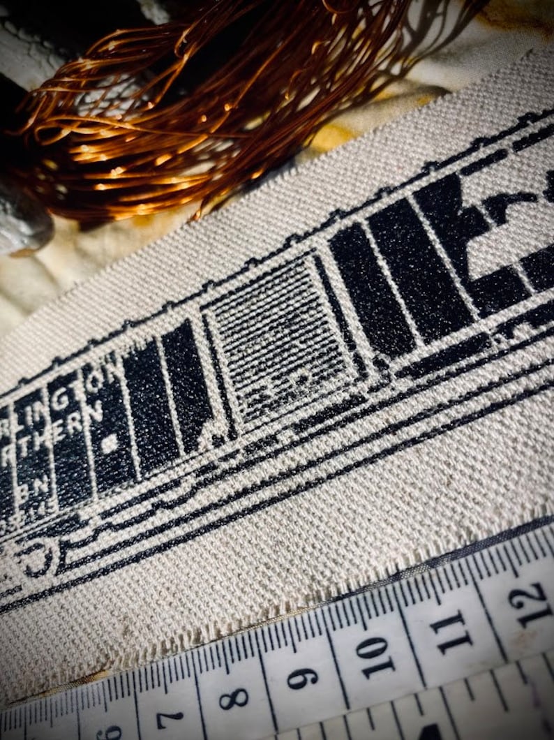 May include: Close-up of a beige fabric with a black train car design and the words "Burlington Northern". A measuring tape is along the bottom edge. Copper wire is in the background.