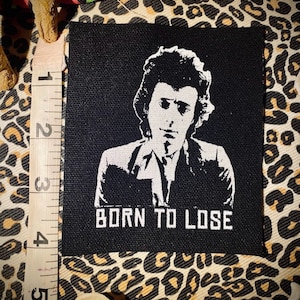 May include: Black and white iron-on patch with a portrait of a man with a quiff hairstyle and the text "BORN TO LOSE".