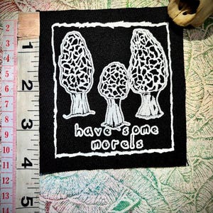 Puede incluir: Parche cuadrado negro con borde blanco que presenta tres setas de colmenilla y el texto "have some morels". El parche mide aproximadamente 10 cm de ancho y 13 cm de alto.