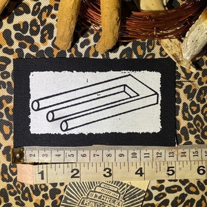 May include: A black and white embroidered patch with a white background and a black outline of a 3D impossible object. The object is a rectangle with two parallel lines extending from the top and bottom of the rectangle. The patch is approximately 3 inches wide and 2 inches tall.