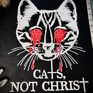 Peut inclure: Patch noir avec un chat blanc aux yeux rouges et du sang qui coule. Les yeux du chat ont des pentagrammes. Le texte sur le patch est "CATS, NOT CHRIST" avec une croix remplaçant le "T" de "CATS" et une croix à la fin de "CHRIST".