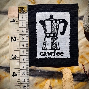 May include: Black and white iron-on patch featuring a drawing of a coffee pot and the word "cawfee" in a stylised font.