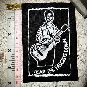 Woody Guthrie scheurt de fascisten neer, naai de punkpatch vast