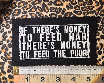 May include: Black rectangular patch with white text: "IF THERE'S MONEY TO FEED WAR THERE'S MONEY TO FEED THE POOR." The patch is on a leopard print background. A ruler shows the patch is about 5 inches wide.