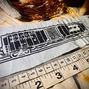 May include: Black and white image of a Burlington Northern train car with the number 23 on the side. The image is printed on a white fabric with a ruler measuring 13 inches.
